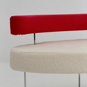 K&ouml;nnte beinhalten: Ein Sofa mit einer cremefarbenen, strukturierten Sitzfl&auml;che in ovaler Form im Boucl&eacute;-Stil. Eine lange, horizontale, rote R&uuml;ckenlehne ist &uuml;ber der Sitzfl&auml;che angebracht und wird von d&uuml;nnen, vertikalen Stangen aus poliertem Chrommetall gest&uuml;tzt.
