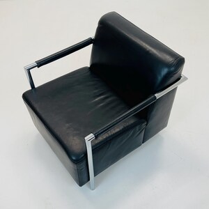 May include: Black leather armchair with chrome frame and arms. The chair has a square seat and back.