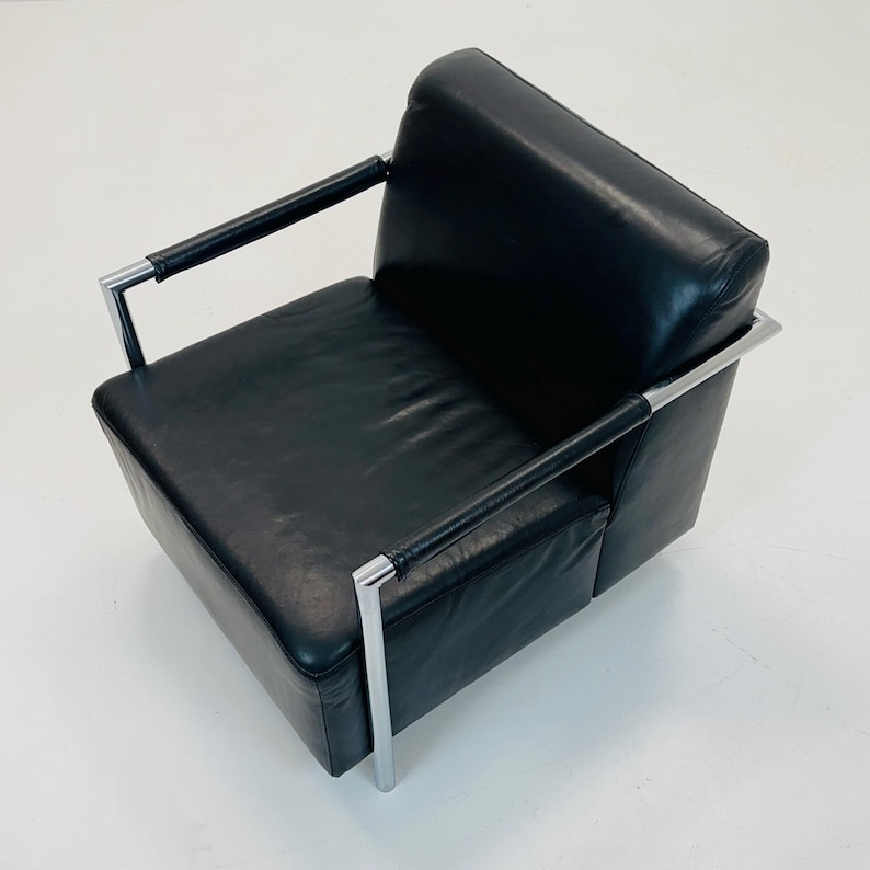 May include: Black leather armchair with chrome frame and arms. The chair has a square seat and back.