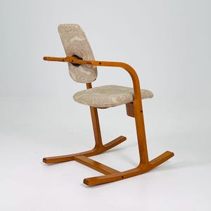 Pode incluir: Uma cadeira de madeira de estilo moderno de meados do s&eacute;culo com uma estrutura curva e assento e encosto de tecido estampado. A cadeira tem apoios de bra&ccedil;os e uma base de balancim &uacute;nica. A madeira tem um acabamento quente e natural.