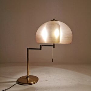 May include: A gold-toned table lamp with a white, dome-shaped shade. The lamp has a flexible arm and a round base.