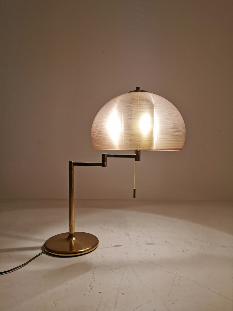 May include: A gold-toned table lamp with a white, dome-shaped shade. The lamp has a flexible arm and a round base.