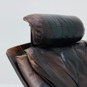 May include: A brown leather armchair with a dark wood frame and a matching headrest. The chair has a worn, vintage look.