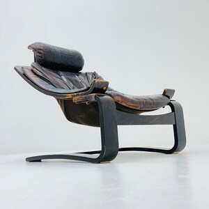May include: A brown leather lounge chair with a curved wooden frame. The chair has a headrest and a footrest.