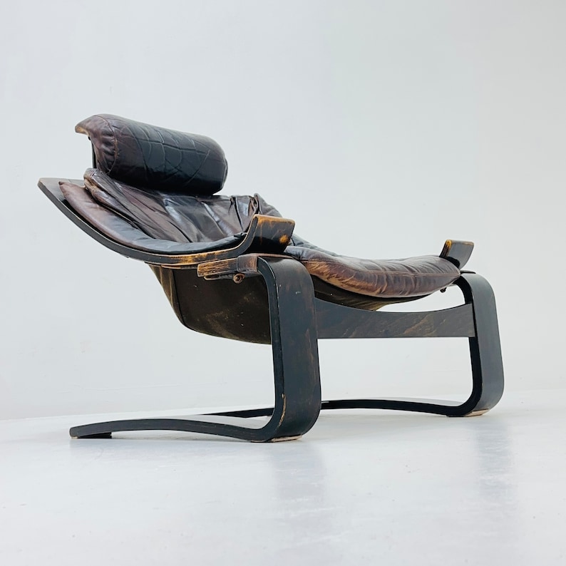 May include: A brown leather lounge chair with a curved wooden frame. The chair has a headrest and a footrest.