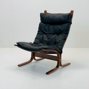 Puede incluir: Un sill&oacute;n lounge de cuero negro con estructura de madera. El sill&oacute;n tiene un asiento y respaldo acolchados, y un dise&ntilde;o curvo y de perfil bajo.