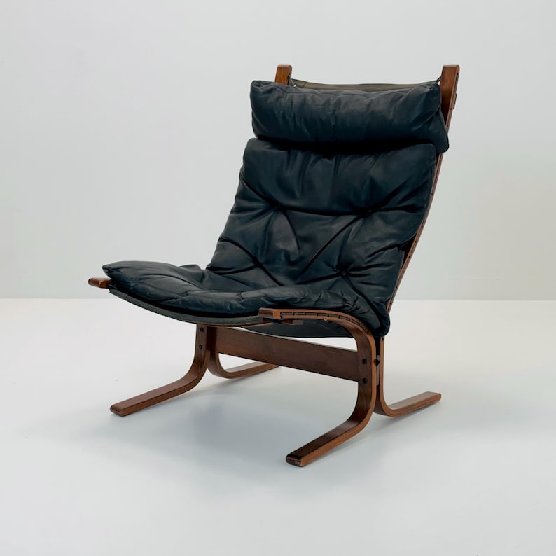 Puede incluir: Un sill&oacute;n lounge de cuero negro con estructura de madera. El sill&oacute;n tiene un asiento y respaldo acolchados, y un dise&ntilde;o curvo y de perfil bajo.