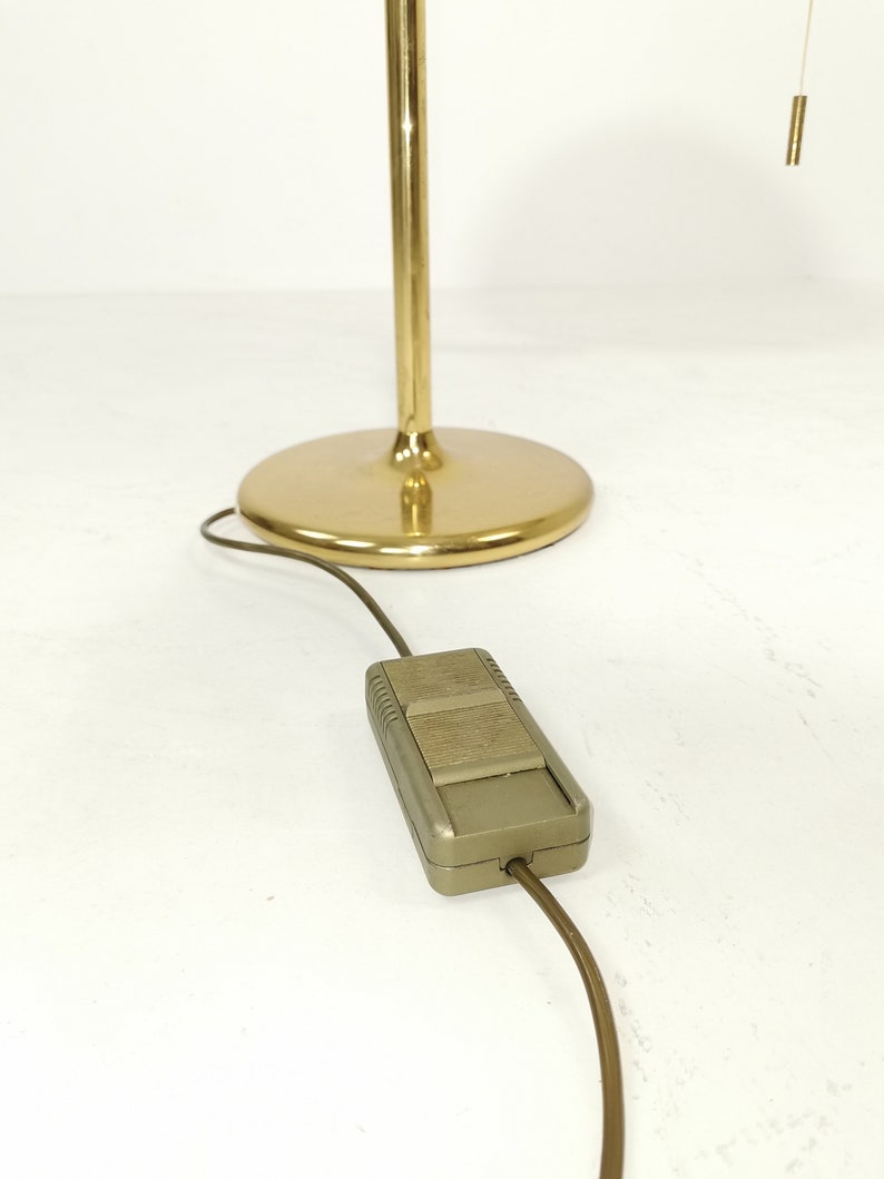 May include: A gold floor lamp with a round base and a cord with a foot switch. The lamp has a pull chain for turning the light on and off.