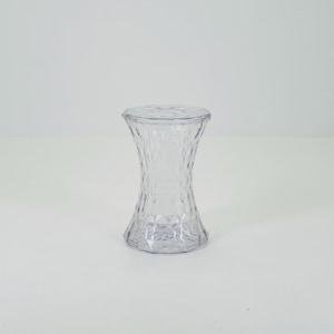Könnte beinhalten: Ein klarer, transparenter Kunststoffhocker mit rautenförmiger Textur. Der Hocker hat eine runde Ober- und Unterseite mit einem körper in Sanduhrform. Das Design ist modern und minimalistisch.