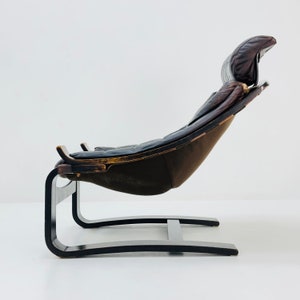 May include: A brown leather lounge chair with a curved wooden frame and a black metal base. The chair has a high back and a comfortable, padded seat.