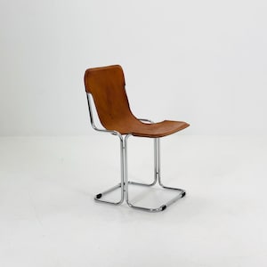 May include: A mid-century modern chair with a brown leather seat and backrest. The chair has a chrome-plated steel frame. The seat is approximately 18 inches wide and 16 inches deep.