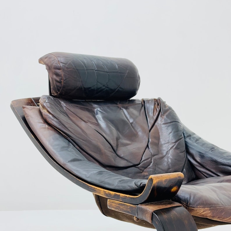 May include: A brown leather armchair with a curved wooden frame and a matching headrest. The chair has a worn, vintage look.