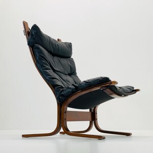 Puede incluir: Un sill&oacute;n lounge de cuero negro con estructura de madera. El sill&oacute;n tiene un respaldo curvo y un asiento amplio. El sill&oacute;n est&aacute; dise&ntilde;ado en un estilo moderno.