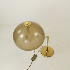 May include: A gold table lamp with a brown glass globe shade. The lamp has a round base and a single switch on the cord.