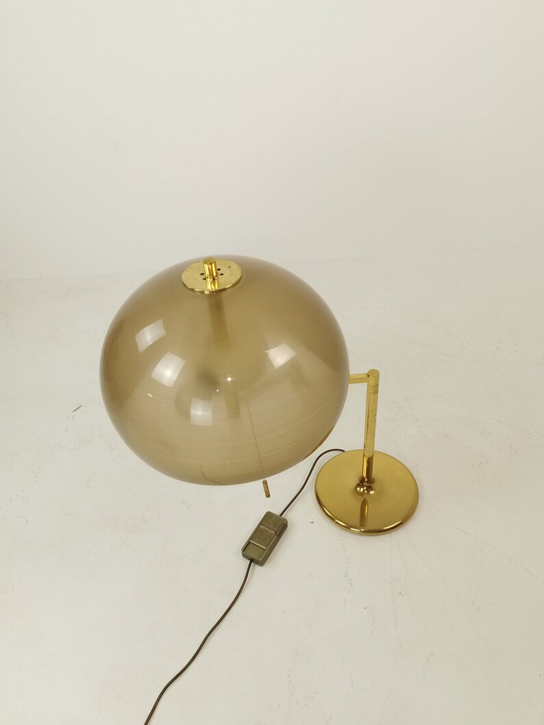 May include: A gold table lamp with a brown glass globe shade. The lamp has a round base and a single switch on the cord.