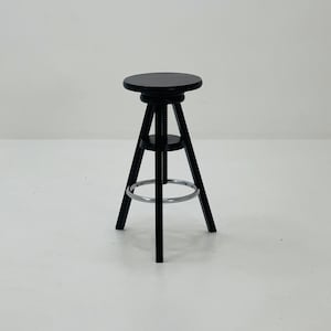 Pode incluir: Um banquinho de bar preto ajustável em altura com um assento redondo e um apoio para os pés de metal.