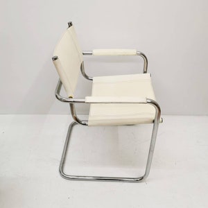 Könnte beinhalten: Ein weißer Lederstuhl mit einem verchromten Gestell. Der Stuhl hat ein schlichtes Design mit einer gebogenen Rückenlehne und Armlehnen.