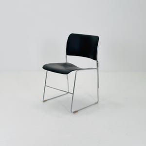 Puede incluir: Una silla negra con asiento y respaldo curvos. La silla tiene una estructura metálica cromada con cuatro patas. La silla está diseñada para sentarse y es adecuada para diversos entornos, como una oficina o un comedor.