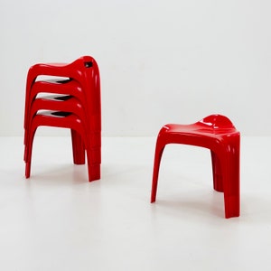 Puede incluir: Un conjunto de cuatro taburetes rojos de plástico apilados y un taburete rojo individual. Los taburetes tienen un asiento curvo y cuatro patas. Los taburetes son de plástico brillante.