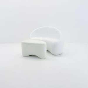 May include: A modern white chair and matching ottoman set. The chair has a curved back and rounded seat, while the ottoman is a low, rectangular shape. Both pieces have a glossy finish and are set against a white background.