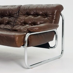 May include: A brown leather sofa with a tufted design and chrome legs. The sofa has a modern style and is in good condition.