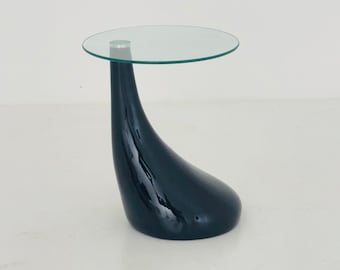 Könnte beinhalten: Ein schwarzer Beistelltisch mit einer runden Glasplatte. Der Tisch hat ein einzigartiges, geschwungenes Design.