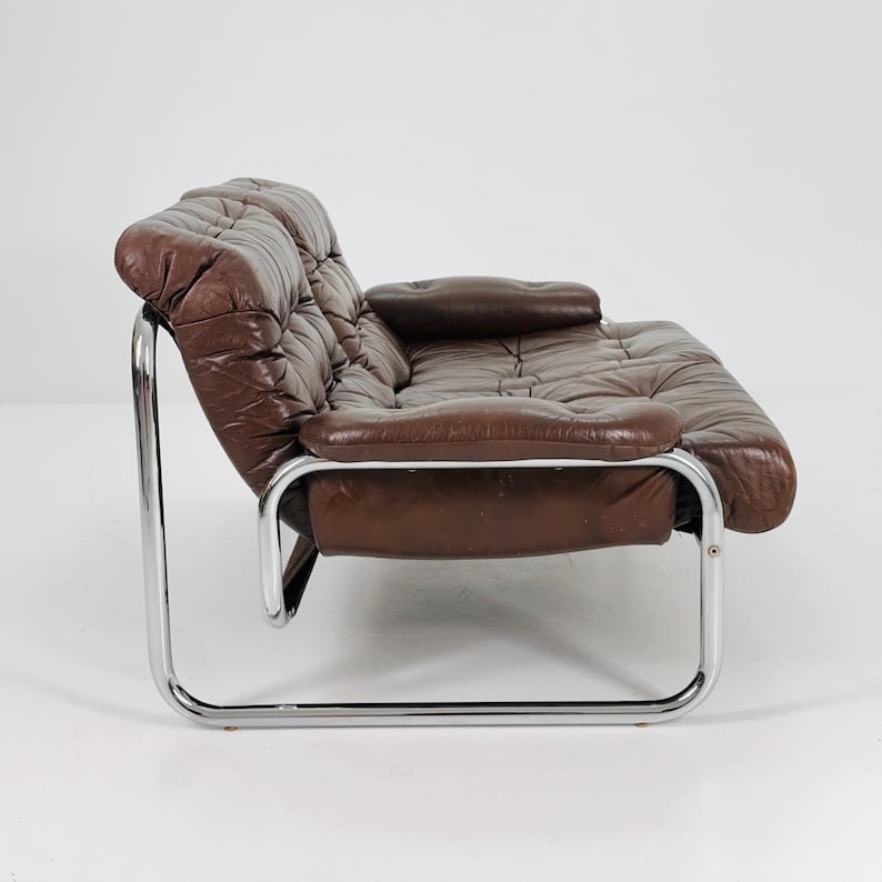 May include: A brown leather sofa with a chrome frame. The sofa has a tufted design and a single armrest.