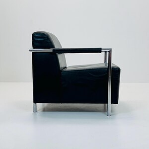 May include: A black leather armchair with a chrome frame. The chair has a simple, modern design with a low back and wide seat.