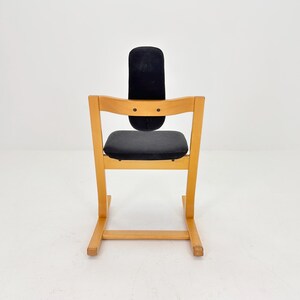May include: A wooden high chair with a black seat and backrest. The chair has a light wood frame and a curved back. The seat and backrest are upholstered in a dark fabric. The chair is designed for a child.