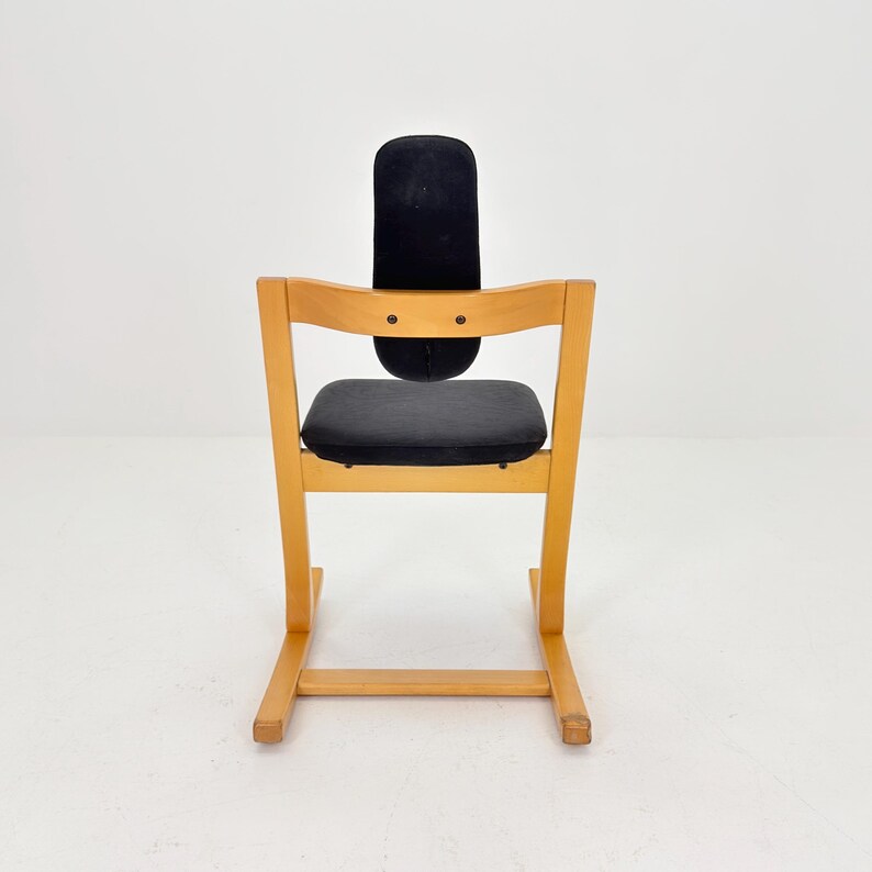 May include: A wooden high chair with a black seat and backrest. The chair has a light wood frame and a curved back. The seat and backrest are upholstered in a dark fabric. The chair is designed for a child.