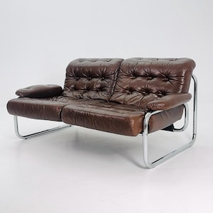May include: A brown leather sofa with a tufted design and a chrome frame. The sofa has a single armrest on the left side.