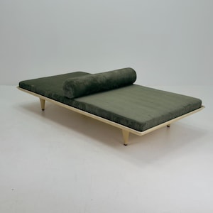 May include: A low-profile daybed featuring a rectangular olive green corduroy cushion and a matching cylindrical bolster pillow. The mattress rests on a light-colored wooden frame supported by four tapered legs with small black feet.