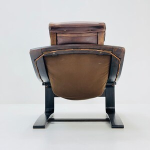 May include: A brown leather and wood armchair with a curved back and a unique, modern design. The chair has a dark brown wooden frame and a brown leather seat and back.