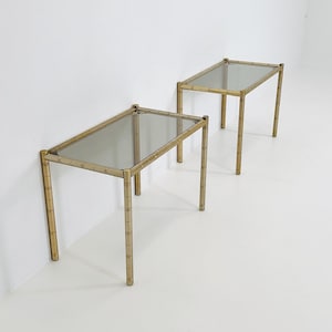 Könnte beinhalten: Zwei goldfarbene Metall-Beistelltische mit Glasplatten. Die Tische haben ein bambusartiges Design an den Beinen.