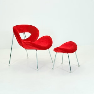 May include: A red velvet chair and footstool set. The chair features a distinctive, open design with a curved back and seat, supported by thin, silver metal legs. The footstool is a smaller, rounded version of the chair, also with silver legs.