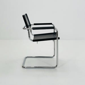 Op de afbeelding: Een moderne zwarte leren stoel met een verchroomd stalen frame. De stoel heeft een cantilever ontwerp met een zitting, rugleuning en armleuningen. De stoel is ontworpen voor comfort en stijl, geschikt voor een woonkamer of kantoor.