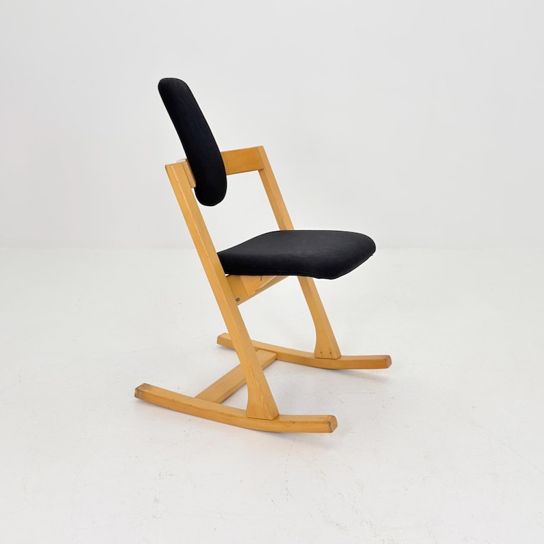 May include: A mid-century modern rocking chair with a black seat and backrest. The chair has a light-colored wooden frame and a curved backrest for added comfort. The chair's design is simple and elegant, suitable for a living room or bedroom.