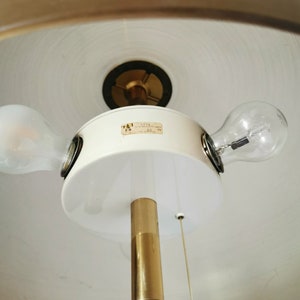 May include: A white and gold floor lamp with two light bulbs. The lamp has a white shade and a gold metal base. The label on the lamp says "127V 60W".