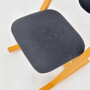 May include: Close-up of a black upholstered chair seat with a subtle pattern. The seat is supported by a light-colored wooden frame. The chair is likely part of a set, with a simple, functional design.
