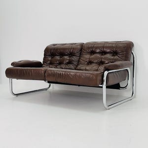 May include: A brown leather sofa with a tufted design and a chrome frame. The sofa has a low profile and a modern style.