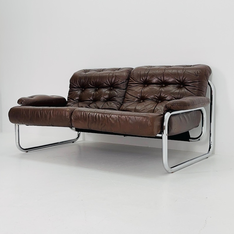 May include: A brown leather sofa with a tufted design and a chrome frame. The sofa has a low profile and a modern style.