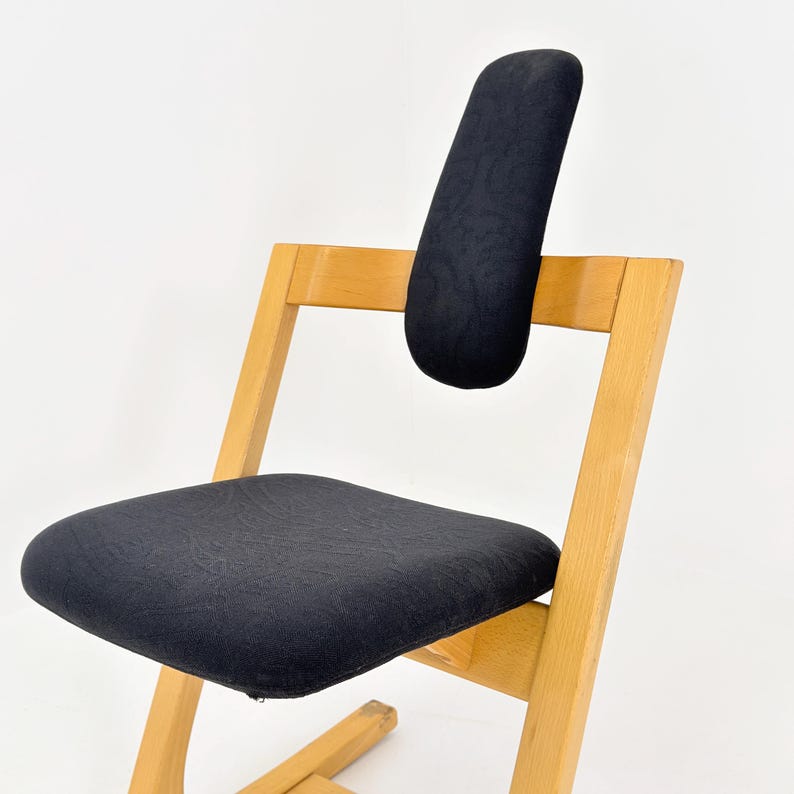 May include: A wooden chair with a black seat and backrest. The chair has a light wood frame and a curved backrest for support. The seat and backrest are upholstered in a dark fabric.
