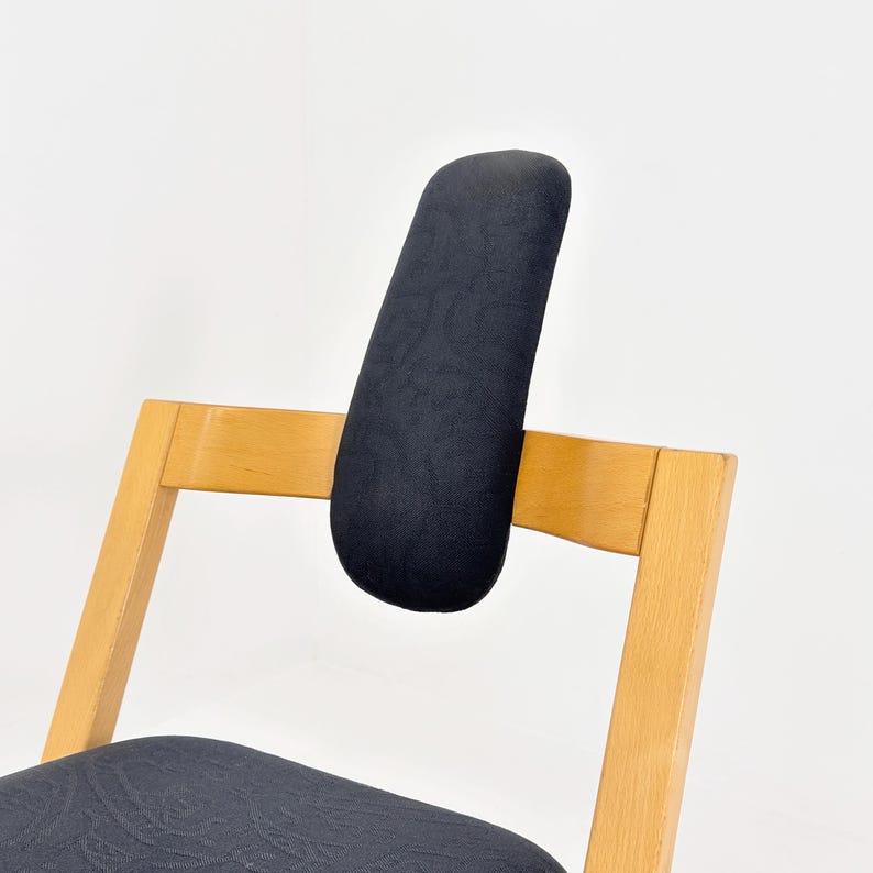 May include: A wooden chair with a black upholstered backrest and seat. The backrest is a curved, padded cushion. The chair's frame is made of light-colored wood. The chair is designed for comfort and support.