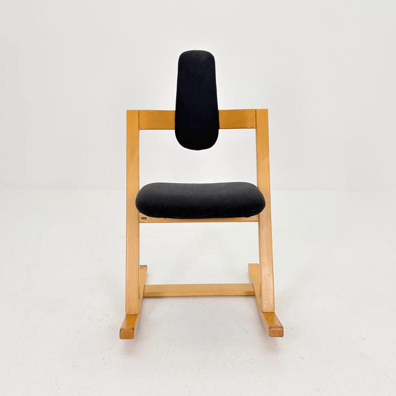 May include: A wooden chair with a black seat and backrest. The chair has a simple, minimalist design with a light-colored wood frame. The backrest is a vertical, padded rectangle.