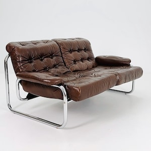 May include: A brown leather two-seater sofa with a chrome frame. The sofa has a tufted design and a relaxed, comfortable look.