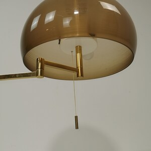 May include: A gold-toned wall lamp with a brown, dome-shaped shade. The lamp has a long, adjustable arm and a pull chain.