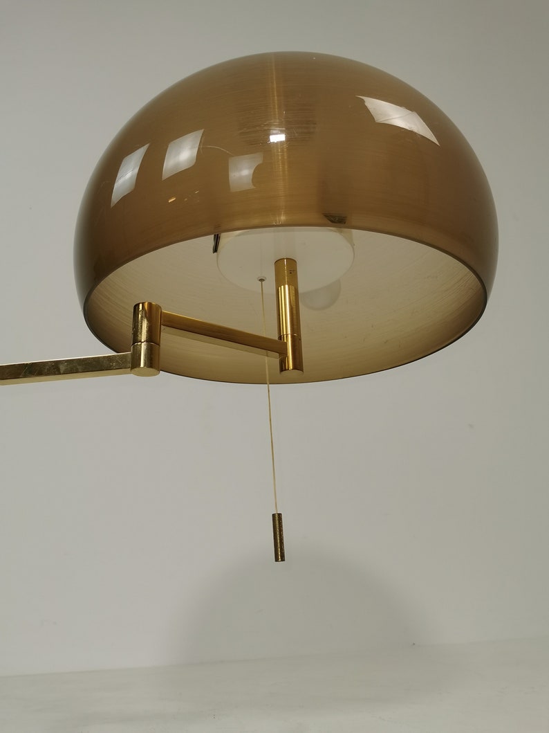 May include: A gold-toned wall lamp with a brown, dome-shaped shade. The lamp has a long, adjustable arm and a pull chain.
