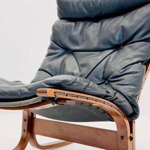 Puede incluir: Un sill&oacute;n de cuero negro con estructura de madera y base curva. El sill&oacute;n tiene un respaldo y un asiento capiton&eacute;.
