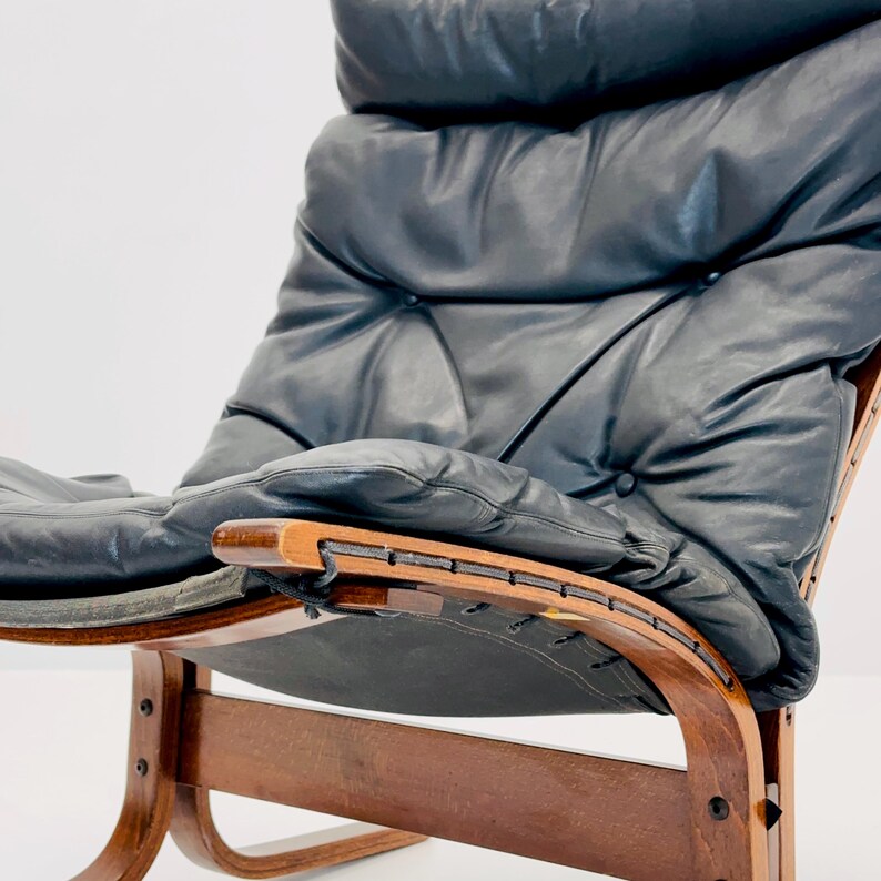 Puede incluir: Un sill&oacute;n de cuero negro con estructura de madera y base curva. El sill&oacute;n tiene un respaldo y un asiento capiton&eacute;.