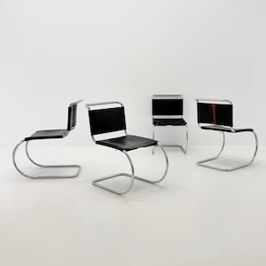 Könnte beinhalten: Vier schwarze Lederstühle mit verchromten Stahlrahmen. Die Stühle haben ein Freischwinger-Design, bei dem Sitz und Rückenlehne von einem durchgehenden, gebogenen Metallrohr getragen werden. Die Stühle sind vor weißem Hintergrund angeordnet.